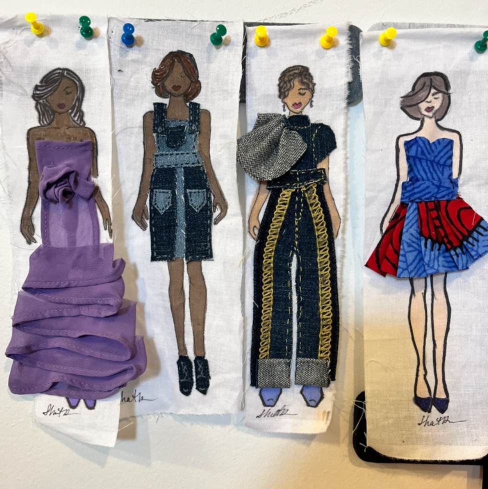 Four paper fashion dolls with different outfits pinned to a board.